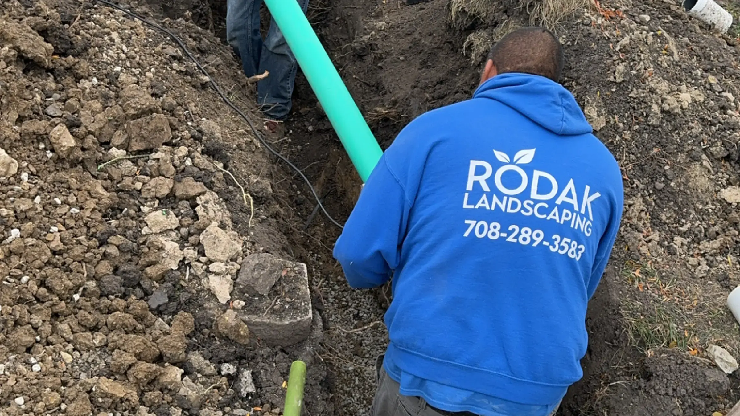 Rodak Landscaping crew installing a drainage pipe in an excavated trench