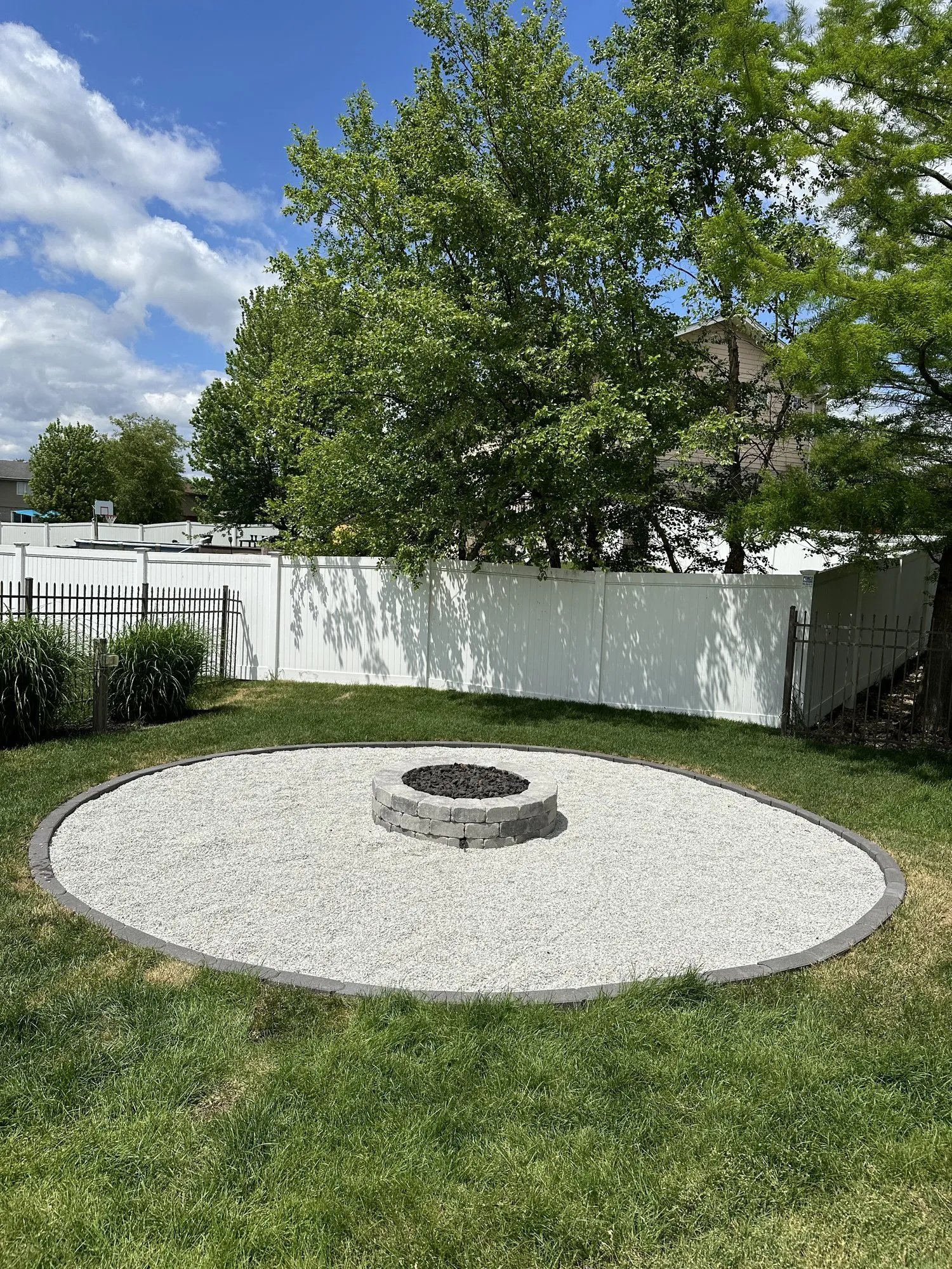 Circular stone fire pit on a bordered crushed-stone pad in a backyard by Rodak Landscaping