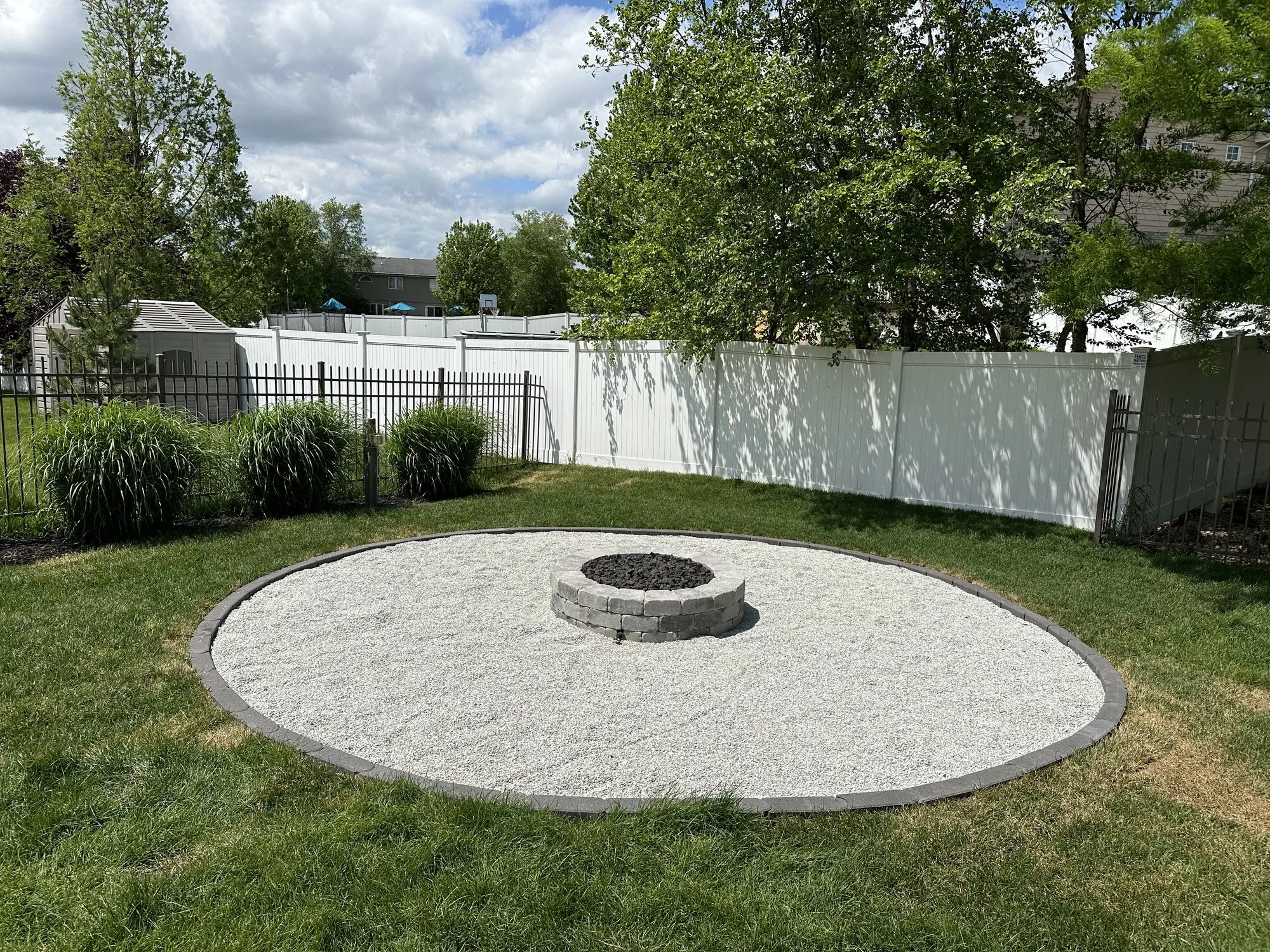 Wide view of a circular stone fire pit on a crushed-stone pad by Rodak Landscaping in Frankfort