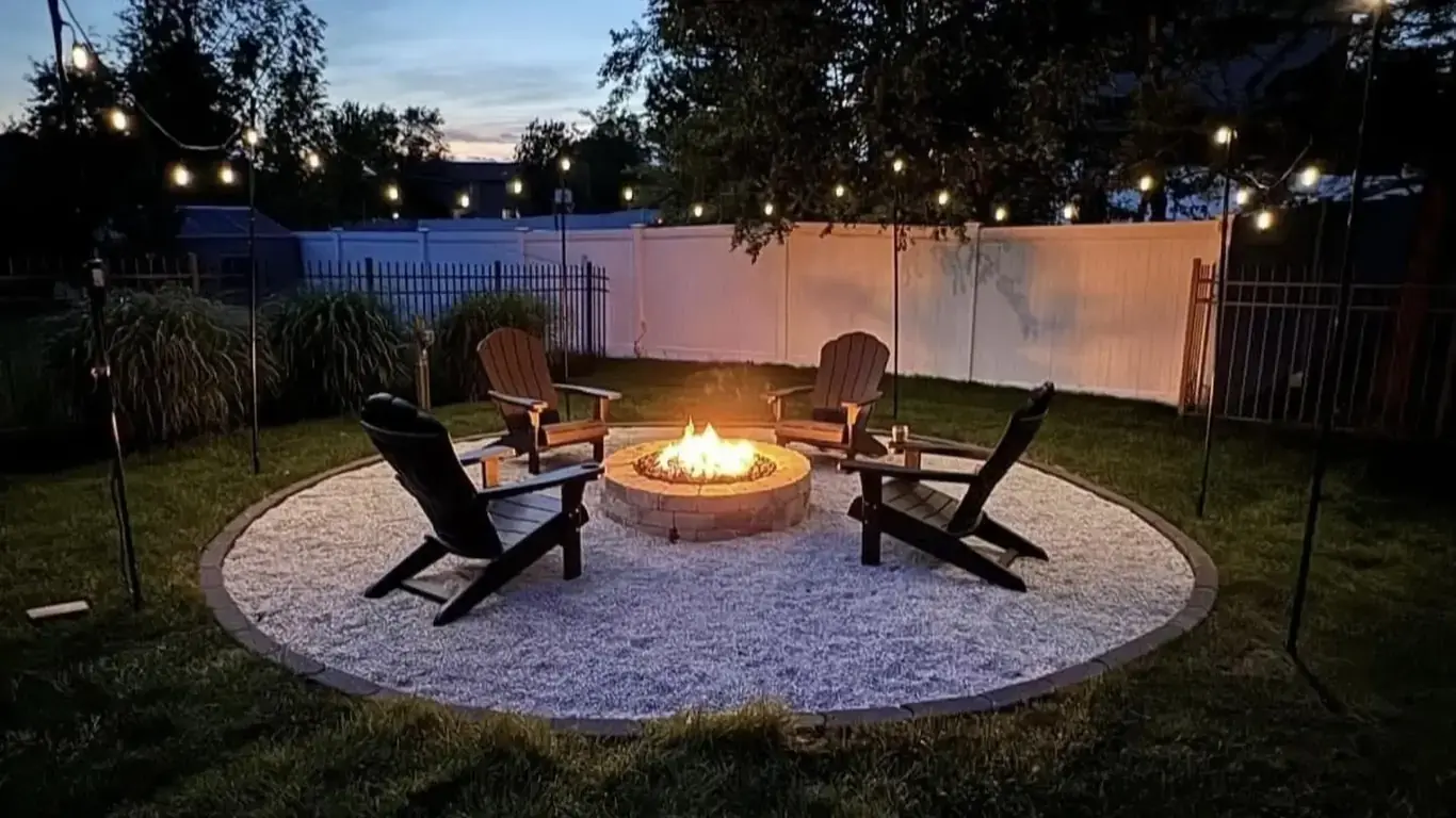 Stone fire pit burning at dusk with Adirondack chairs and string lights, built by Rodak Landscaping in Frankfort