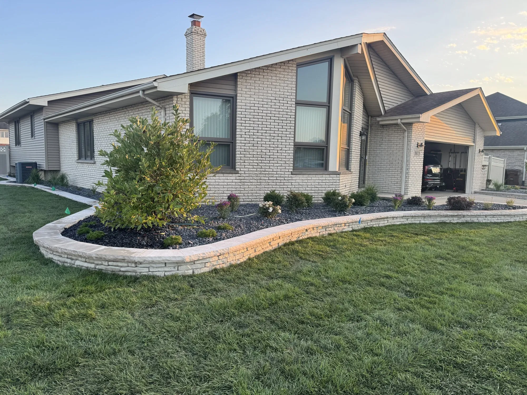 Curved stacked-stone bed wall and planting bed on a front yard by Rodak Landscaping