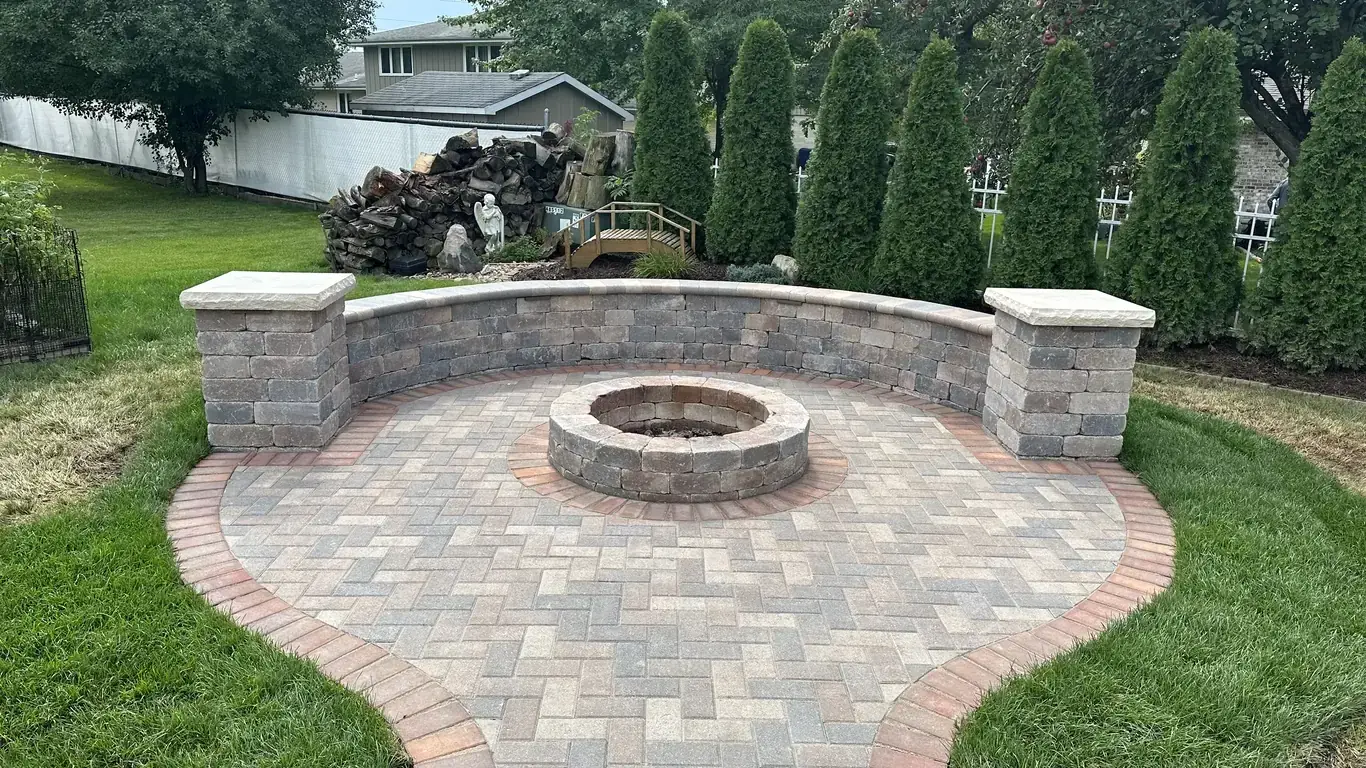 Custom outdoor living space with stone fire pit and curved seating wall by Rodak Landscaping