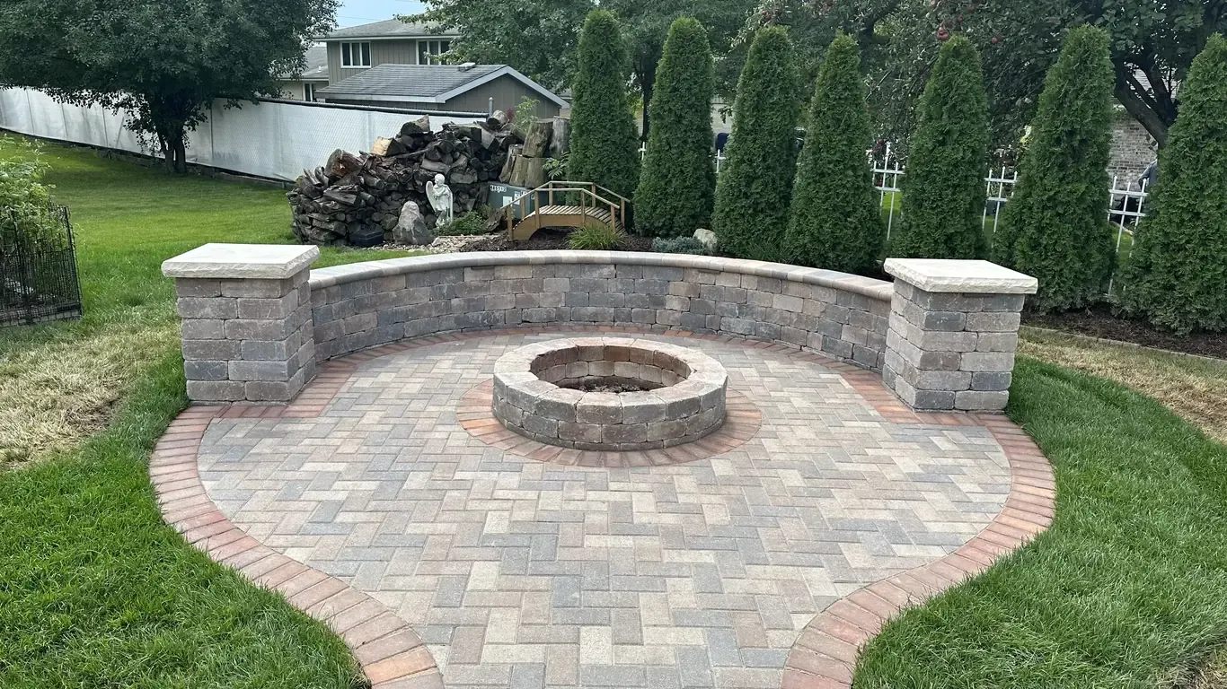 Custom outdoor living space with stone fire pit and curved seating wall by Rodak Landscaping