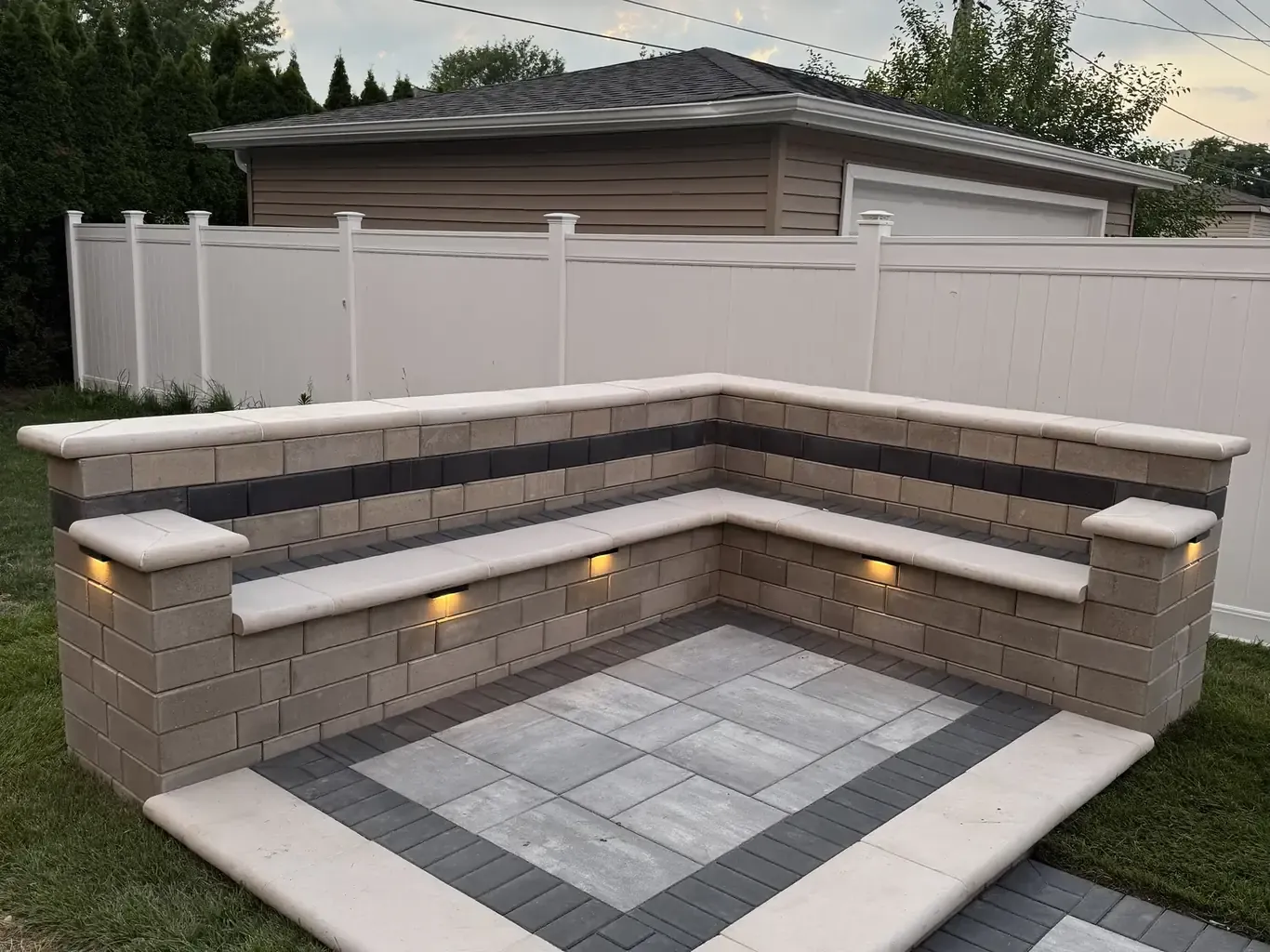 Integrated low-voltage cap lights glowing on a paver patio sitting wall at dusk, installed by Rodak Landscaping